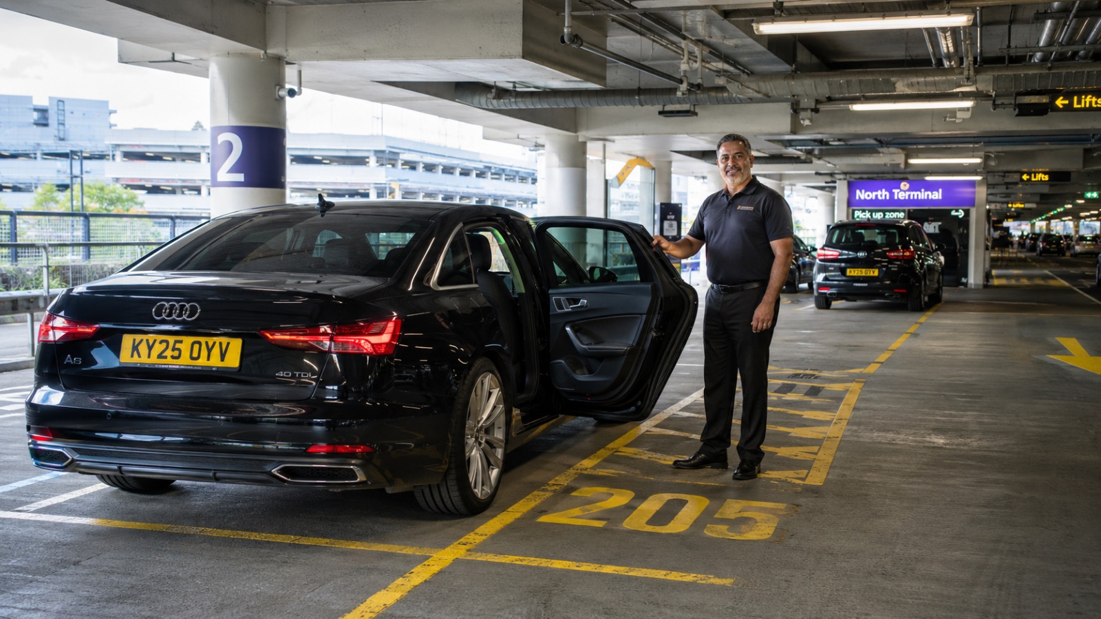 Black saloon taxi waiting in an airport Express Pick Up bay inside a modern multi-storey car park with clean bay markings.