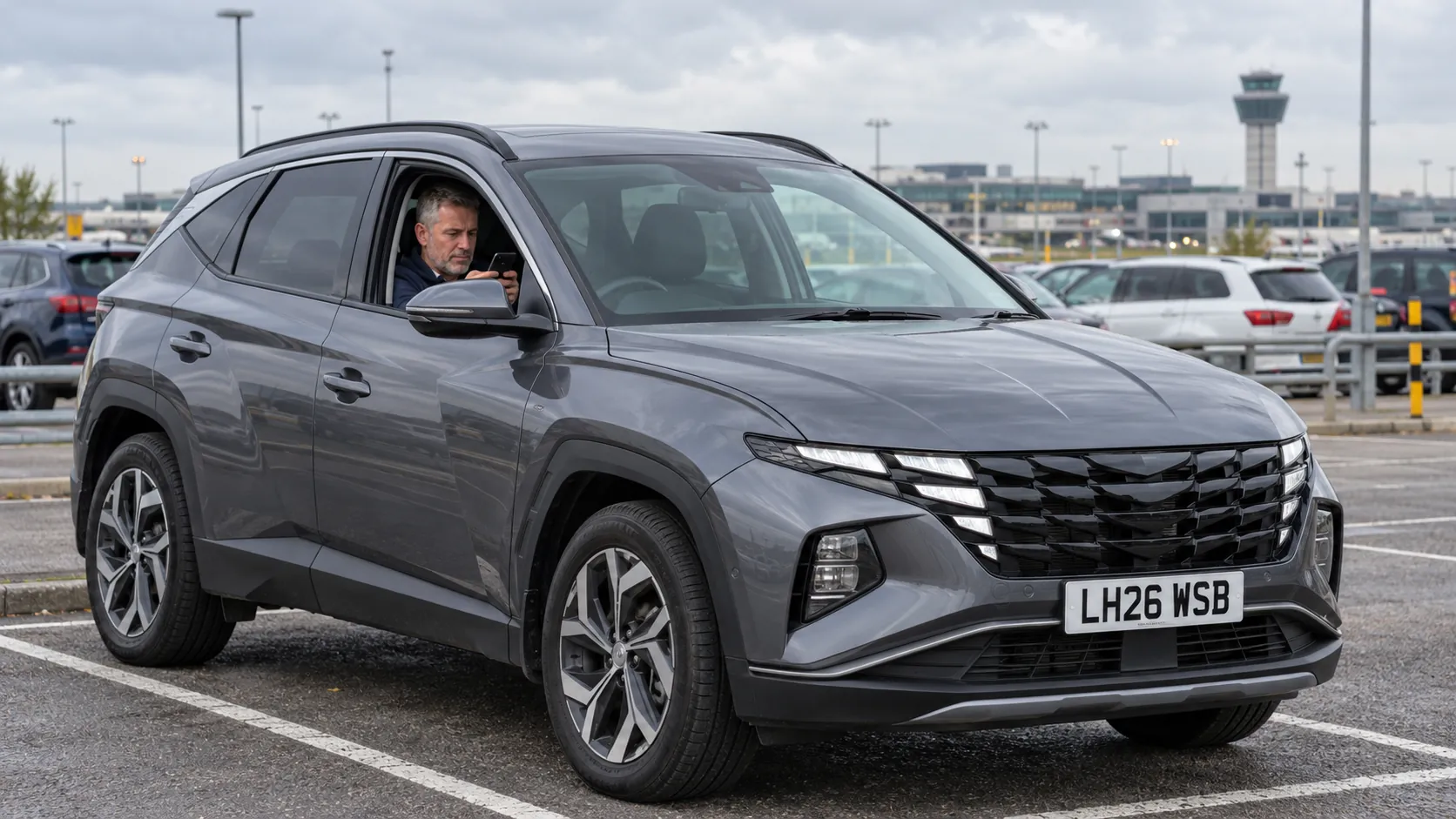 Man waiting in his grey car with his phone in a car park near Heathrow before a pick-up
